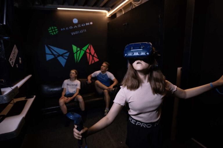 tyttö pelaa virtuaalitodellisuuspeliä lasit päässä, perhe seuraa.