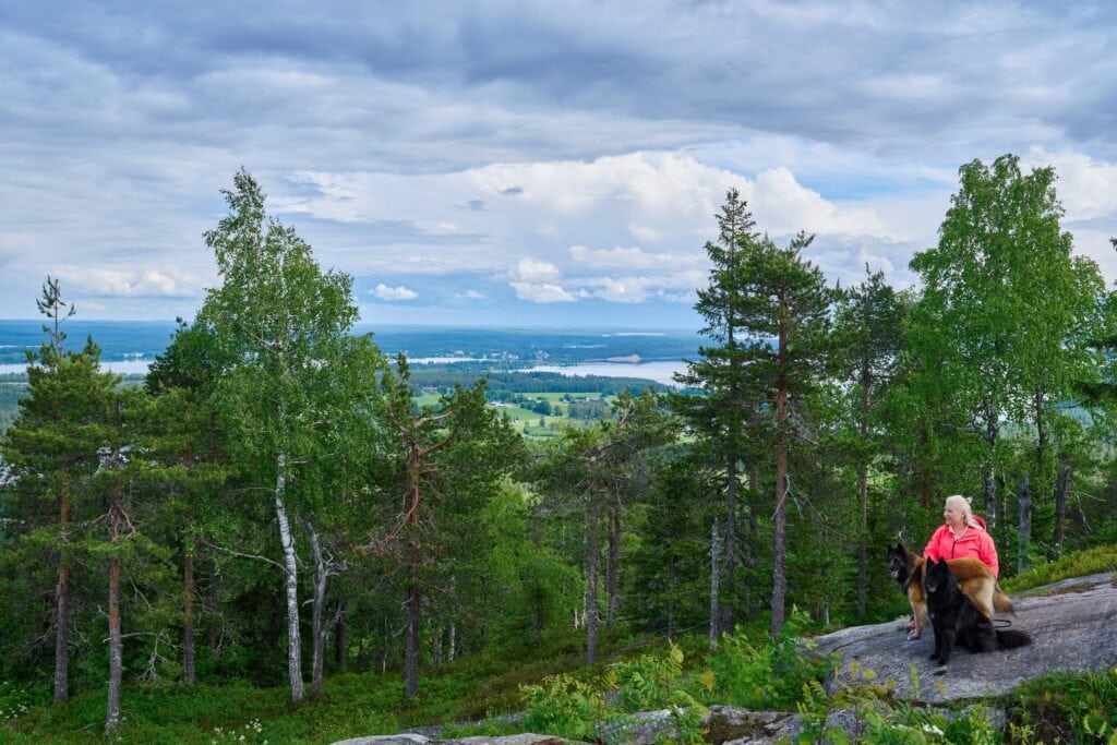 Kuvassa reitkeilyä, nainen ja kaksi koiraa istuu kalliolla Vuokatinvaaralla