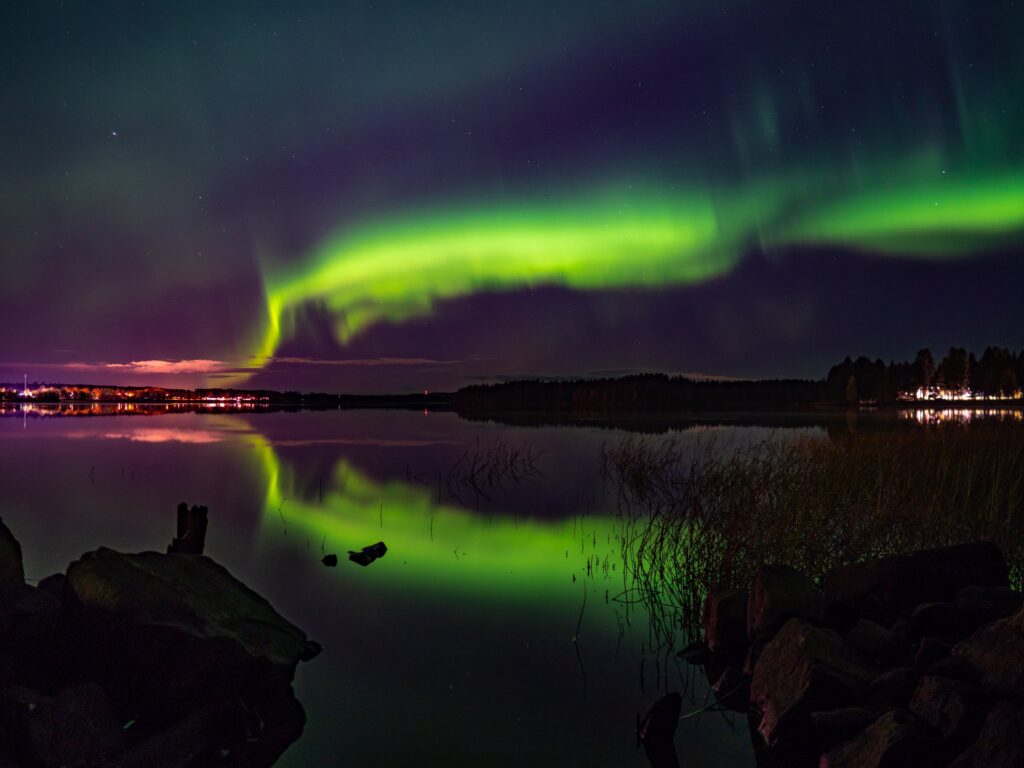 Valokuva revontulista syksyllä järven päällä. Revontulet heijastuvat järvestä.