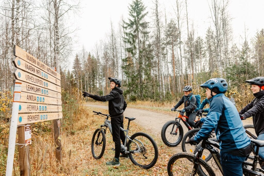 Neljä pyöräilijää tutkimassa reittikylttejä hiekkatiellä.